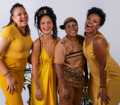 Quatro integrantes do Saraus das Pretas com roupas amarelas. Elas sorriem